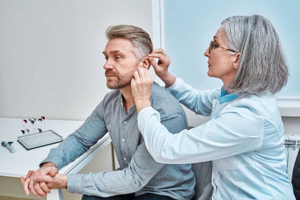 Experienced female doctor fitting Intra-The-Ear hearing aid into patient's ear while consultation in audiology clinic. ITE and ITC hearing aids Experienced female doctor fitting Intra-The-Ear hearing aid into patient's ear while consultation in audiology clinic. ITE and ITC hearing aids hearing aids person stock pictures, royalty-free photos & images