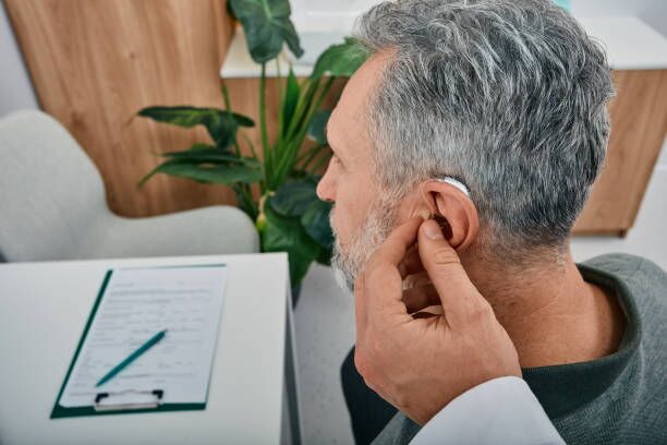 Audiologist fits a hearing aid on deafness mature man ear while visit a hearing clinic. Hearing solutions for older Audiologist fits a hearing aid on deafness mature man ear while visit a hearing clinic. Hearing solutions for older hearing aids stock pictures, royalty-free photos & images