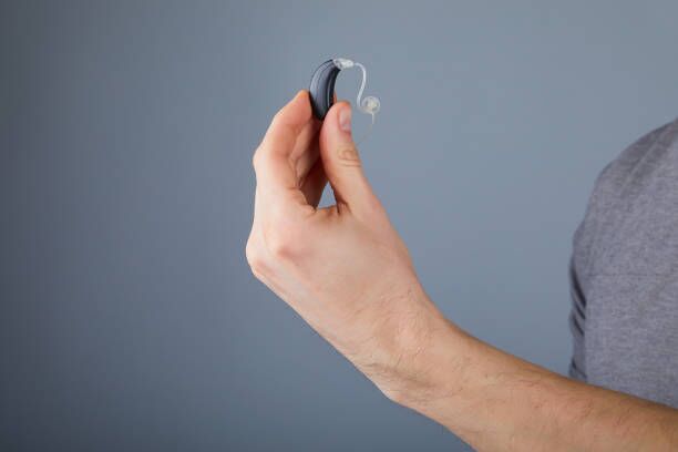 holding small black hearing aid Man holding small black hearing aid, closeup. Hearing aids on grey background, alternative to surgery. hearing aid batteries stock pictures, royalty-free photos & images