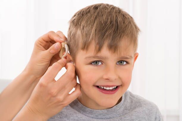 Close-up Of A Smiling Boy With Hearing Aid Close-up Of A Doctor Fitting Hearing Aid On Smiling Boy's Ear child hearing aid stock pictures, royalty-free photos & images